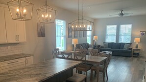 Une cuisine moderne dotée d’un grand îlot central, d’un coin repas avec des chaises en bois et d’un salon avec un canapé et des lampes.