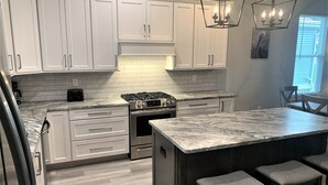 Une cuisine moderne avec des meubles blancs, un plan de travail en marbre, une cuisinière à gaz et un coin bar avec des tabourets.