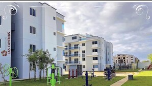 Un edificio residencial de varios pisos, con equipamiento de gimnasia al aire libre y una zona verde.