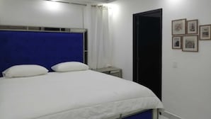 Un dormitorio con una cama, una mesita de noche, una puerta y cuadros en la pared.