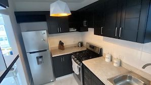 Una cocina moderna con armarios oscuros, un lavamanos de acero inoxidable, una estufa a gas y un refrigerador.