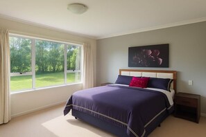 Quarto com uma janela grande, uma cama com cabeceira, uma mesinha de cabeceira e uma obra de arte na parede.