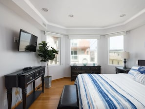 Une chambre à coucher avec un lit, un bureau, une chaise, une plante en pot et une fenêtre.