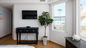 A bedroom with a bed, a desk, a TV, a plant, and a window with a view. - Ocean Front Beach Get Away w/ AC! (San Diego)