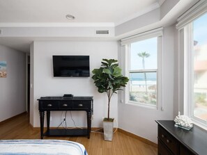 A bedroom with a bed, a desk, a TV, a plant, and a window with a view.