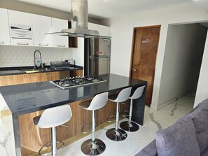 Una cocina moderna con una isla central, taburetes de bar, electrodomésticos de acero inoxidable y una puerta de madera.