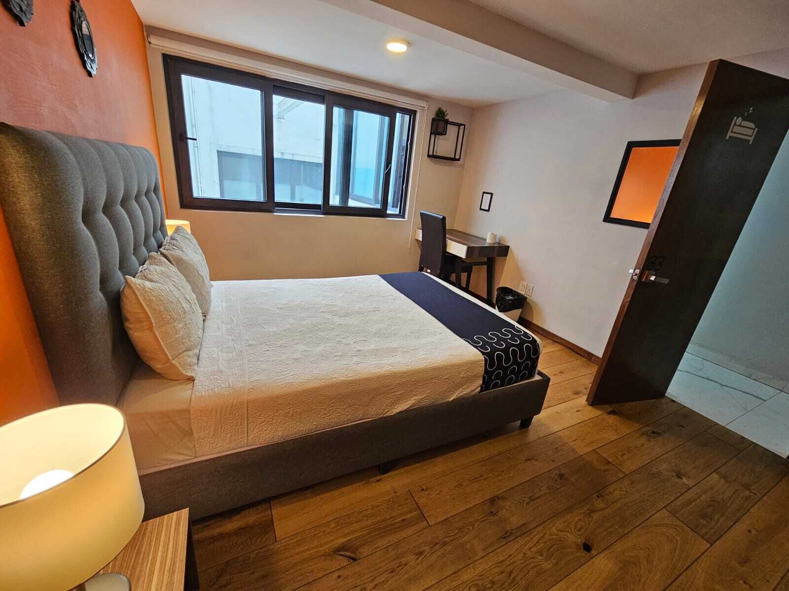Un dormitorio con cama, escritorio, silla, ventana y puerta.