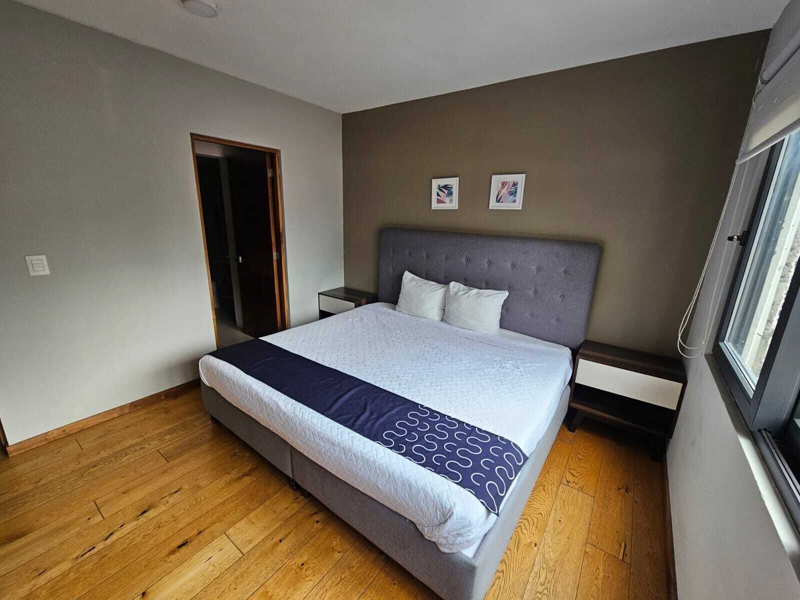 Ein Schlafzimmer mit Bett, Nachttisch, Fenster und Tür.
