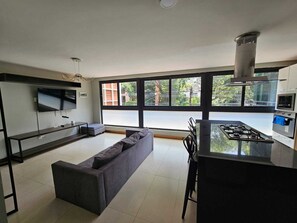 A modern kitchen with a gas stove, a dining area with chairs, a sofa, and a TV mounted on the wall.