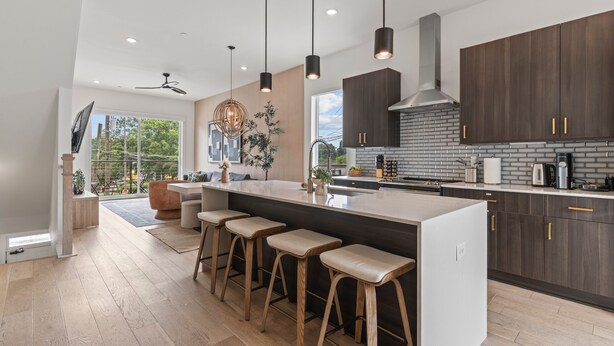 A modern kitchen with a large island, bar stools, dark wooden cabinets, and a view of the outdoors. - Atlanta Rooftop Retreat Sleeps 10 + Parking (Atlanta)