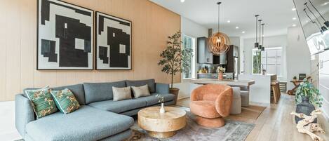 A modern living room with a sectional sofa, a round coffee table, and a dining area in the background.