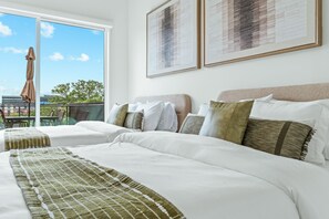Una habitación de hotel con dos camas, un balcón con mesa y sillas, y ventanas amplias.