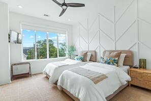 A modern bedroom with two beds, a ceiling fan, a window with a view, and a wall-mounted TV.