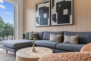 A modern living room with a grey sectional sofa, a round coffee table, and a large window with a view of greenery.