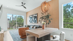 A modern dining area with a wooden table, grey upholstered chairs, a ceiling fan, and a large window with a view of greenery. - Atlanta Rooftop Retreat Sleeps 10 + Parking (Atlanta)
