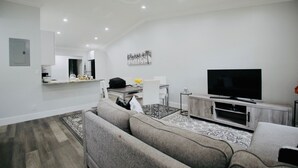 A modern living room with a sofa, a TV, and a dining area with a table and chairs.