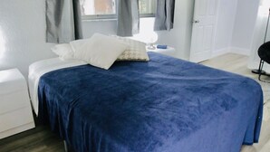 A bedroom with a large bed, a nightstand, a dresser, and a window with curtains.
