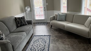 A living room with two sofas, a standing fan, and a patterned rug.