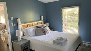 A bedroom with a bed, nightstands, a lamp, a window with blinds, and a ceiling fan.