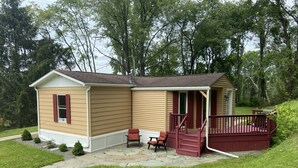 A single-story house with a porch and a small deck, surrounded by a well-maintained lawn and trees.