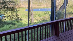 A covered deck with a view of a lake and surrounding greenery.