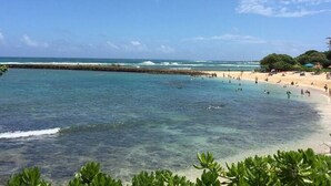 A beach with clear blue water, a sandy shore, and some greenery in the foreground. - SEArider ONE at Turtle Bay (2 bedroom / 2 bath) (Kahuku)