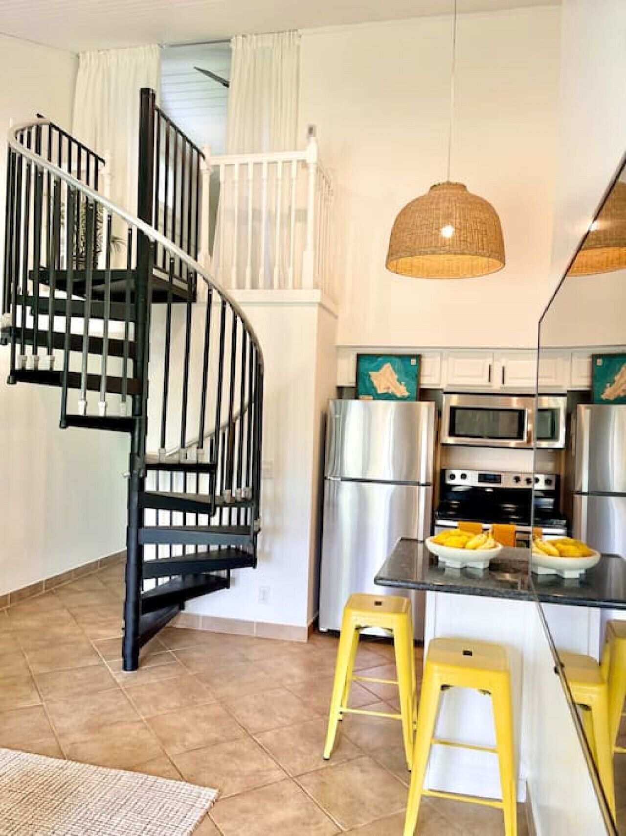 Une cuisine compacte dotée d’appareils électroménagers modernes, un petit coin repas avec des tabourets jaunes et un escalier en colimaçon noir.