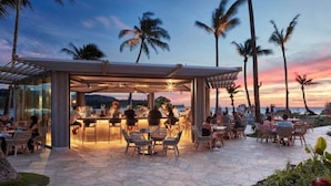 An outdoor bar area with seating, palm trees, and a view of the ocean at sunset. - SEArider ONE at Turtle Bay (2 bedroom / 2 bath) (Kahuku)