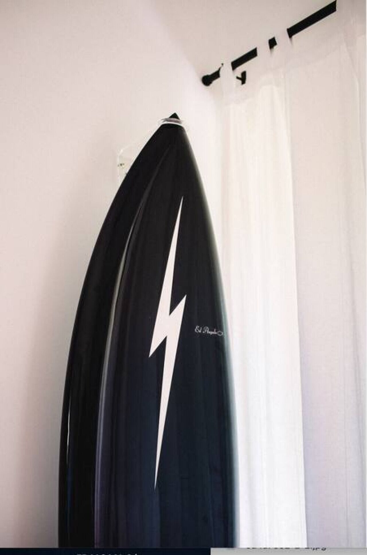 Una tabla de surf apoyada contra una pared en una habitación con una cortina blanca.