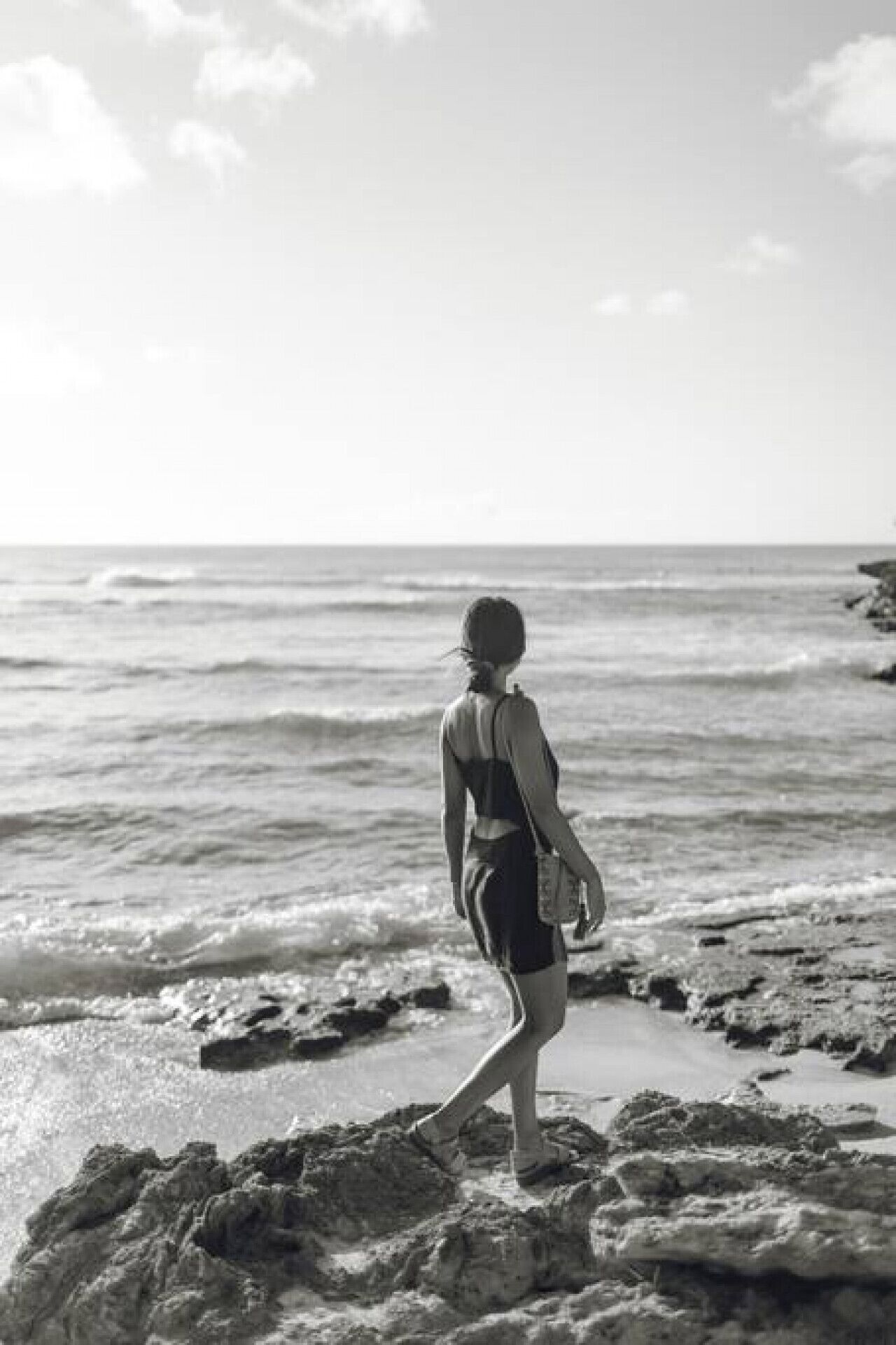 Eine Person steht auf einem felsigen Strand, im Hintergrund das Meer.