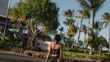 A person walking on a paved path with palm trees and a sign that reads "TURING" in the background.
