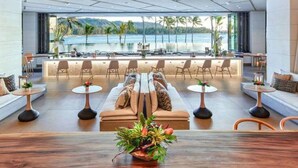 A modern lounge area with a sofa, chairs, and tables, overlooking a pool and palm trees. - SEArider ONE at Turtle Bay (2 bedroom / 2 bath) (Kahuku)