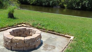 Un pozo de fuego circular de piedra en un área verde con un río al fondo.