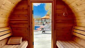 Una sauna con bancos de madera y una puerta de vidrio que da a un área exterior con piscina y sillas de descanso.