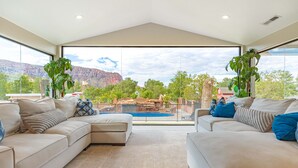 Un salón espacioso con dos sofás color beige, un ventanal con vistas a montañas y una piscina.