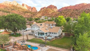 Una casa grande con piscina, rodeada por un patio cercado y con vistas a una montaña.