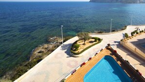 A pool area with clear blue water, a rocky shoreline, and a large rock formation in the background. - Orellana by Interhome (Calpe/Calp)