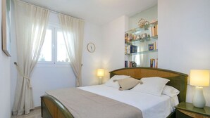 A neatly made bed with a wooden headboard, a bedside table with a lamp, and a bookshelf against the wall. - Orellana by Interhome (Calpe/Calp)