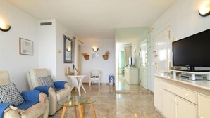 A modern living room with a sofa, armchairs, a glass coffee table, a TV, and a kitchen area with cabinets and a countertop. - Orellana by Interhome (Calpe/Calp)