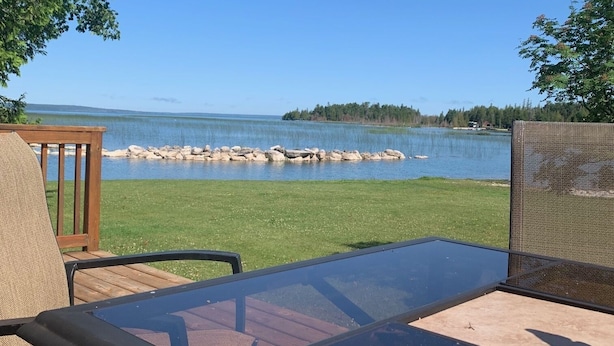 Terassi, jossa on lasipöytä ja -tuolit, ja josta avautuu näkymä järvelle, jonka rannalla on kivikkoista maastoa ja kauempana horisontissa saari.