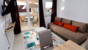 Ein Wohnzimmer mit einer Couch, einem Fernseher, einem Tisch und einem Sessel.