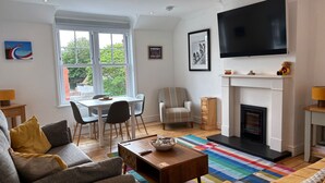 A living room with a fireplace, a television, a dining area, and a sofa. - Seafront Sheringham 1 bed Apt sleeps 4 - 1xdog (SHERINGHAM)