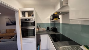 A compact kitchen with built-in appliances, a microwave, and a sink. - Seafront Sheringham 1 bed Apt sleeps 4 - 1xdog (SHERINGHAM)