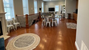 Un vaste espace de vie doté d’un plancher en bois, de meubles blancs, d’une cheminée et d’un coin repas avec une table et des chaises.