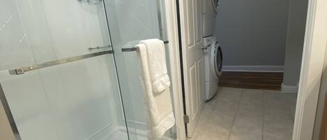 Ein Badezimmer mit Duschkabine aus Glas, einer Waschmaschine und Fliesenboden.