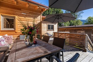 Eine Holzhütte mit einer Terrasse, einem Tisch, Stühlen und einem großen Sonnenschirm.