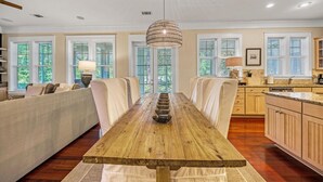 Un'ampia sala da pranzo con un lungo tavolo in legno, sedute imbottite e grandi finestre dotate di tende.