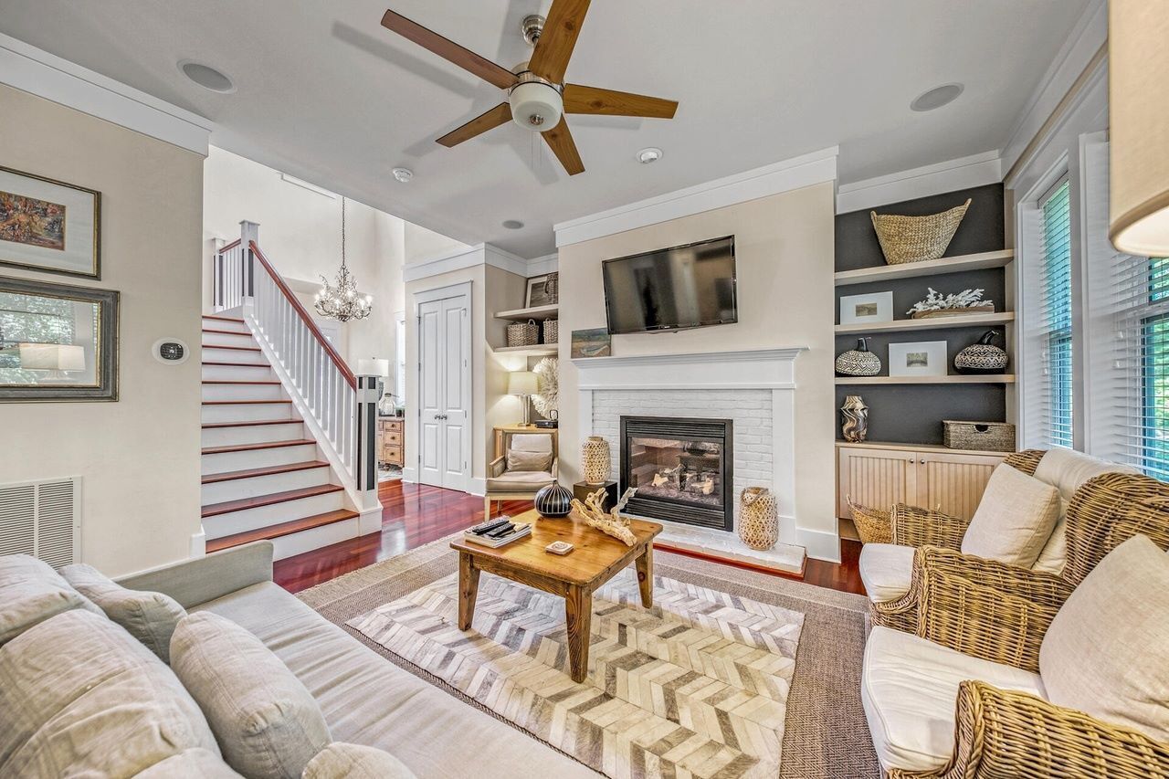 A spacious living room with a fireplace, a ceiling fan, and a staircase leading to another level.