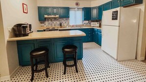 Une cuisine de taille réduite avec des meubles de couleur turquoise, un réfrigérateur blanc et un sol à motifs.