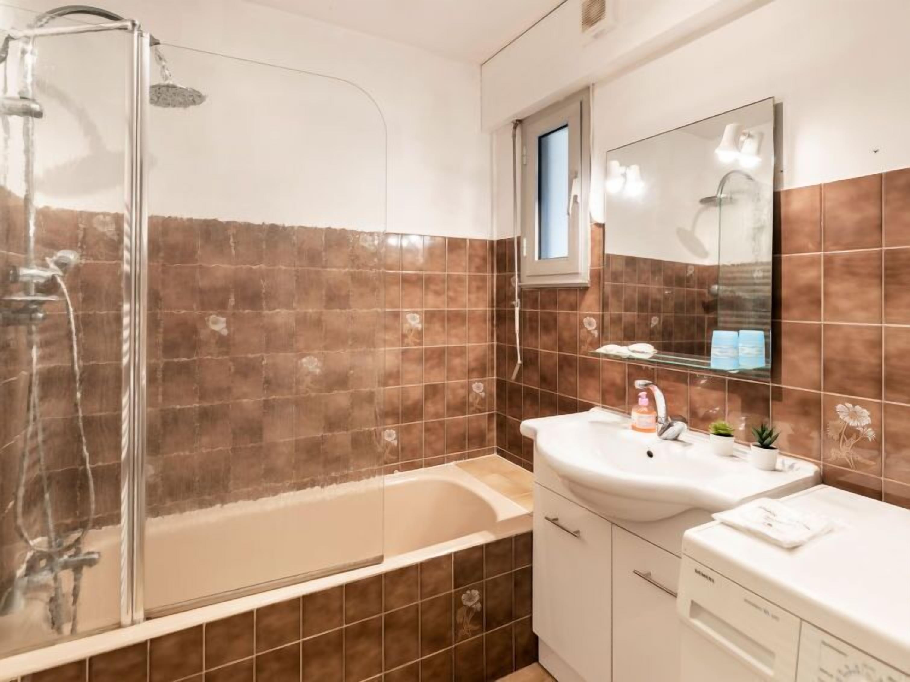 A bathroom with a glass shower enclosure, a bathtub, a sink with a mirror above it, and a small window.